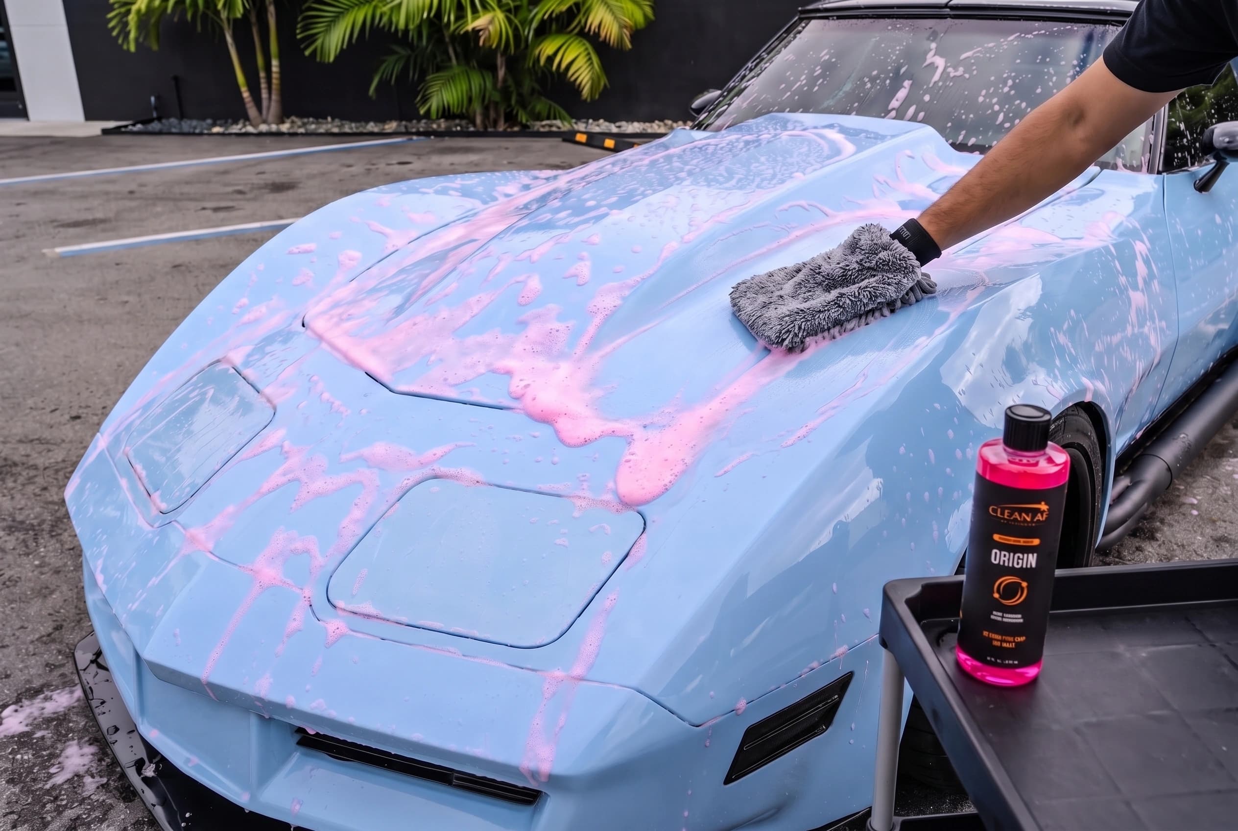 A wash mitt washing the wet, foamed hood of the light-blue Corvette