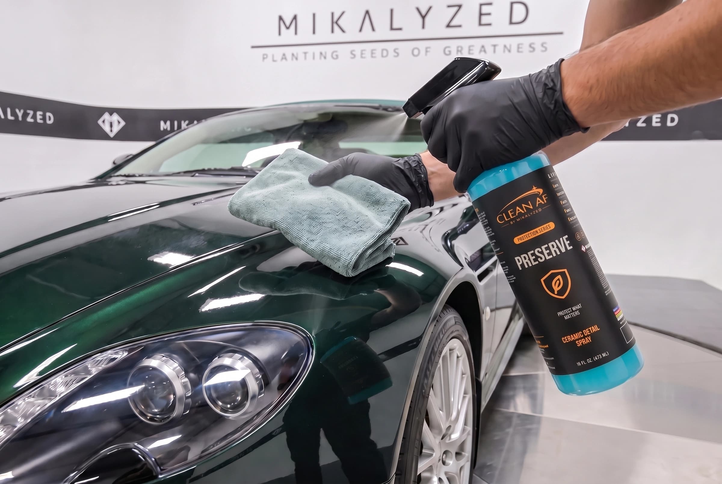 PRESERVE spraying toward a microfiber towel held above the green Aston Martin hood