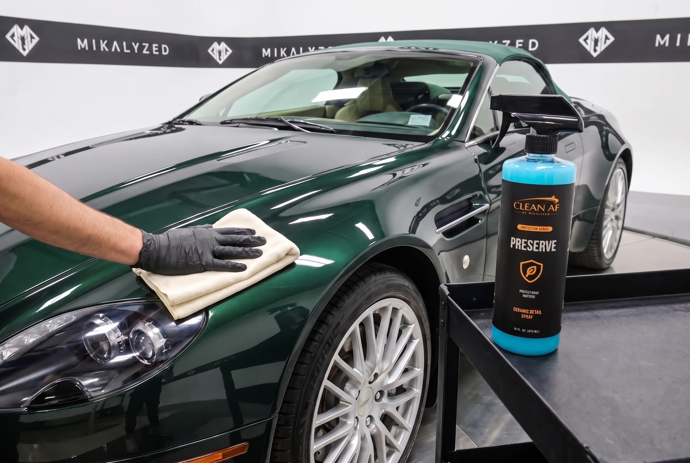 A second, ivory microfiber towel buffing the green Aston Martin hood beside PRESERVE
