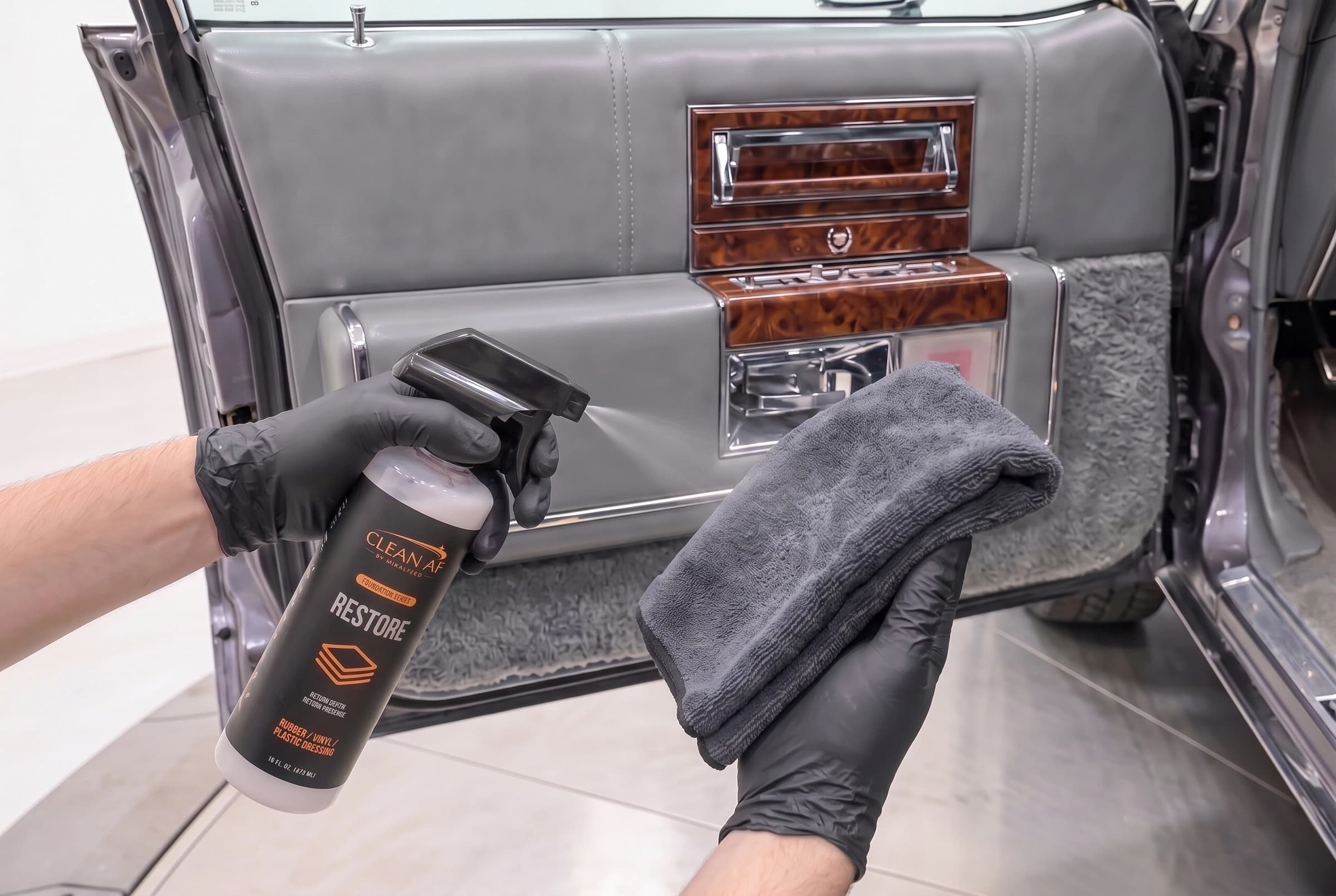 The black RESTORE trigger spraying toward a raised charcoal microfiber towel beside the gray Cadillac door