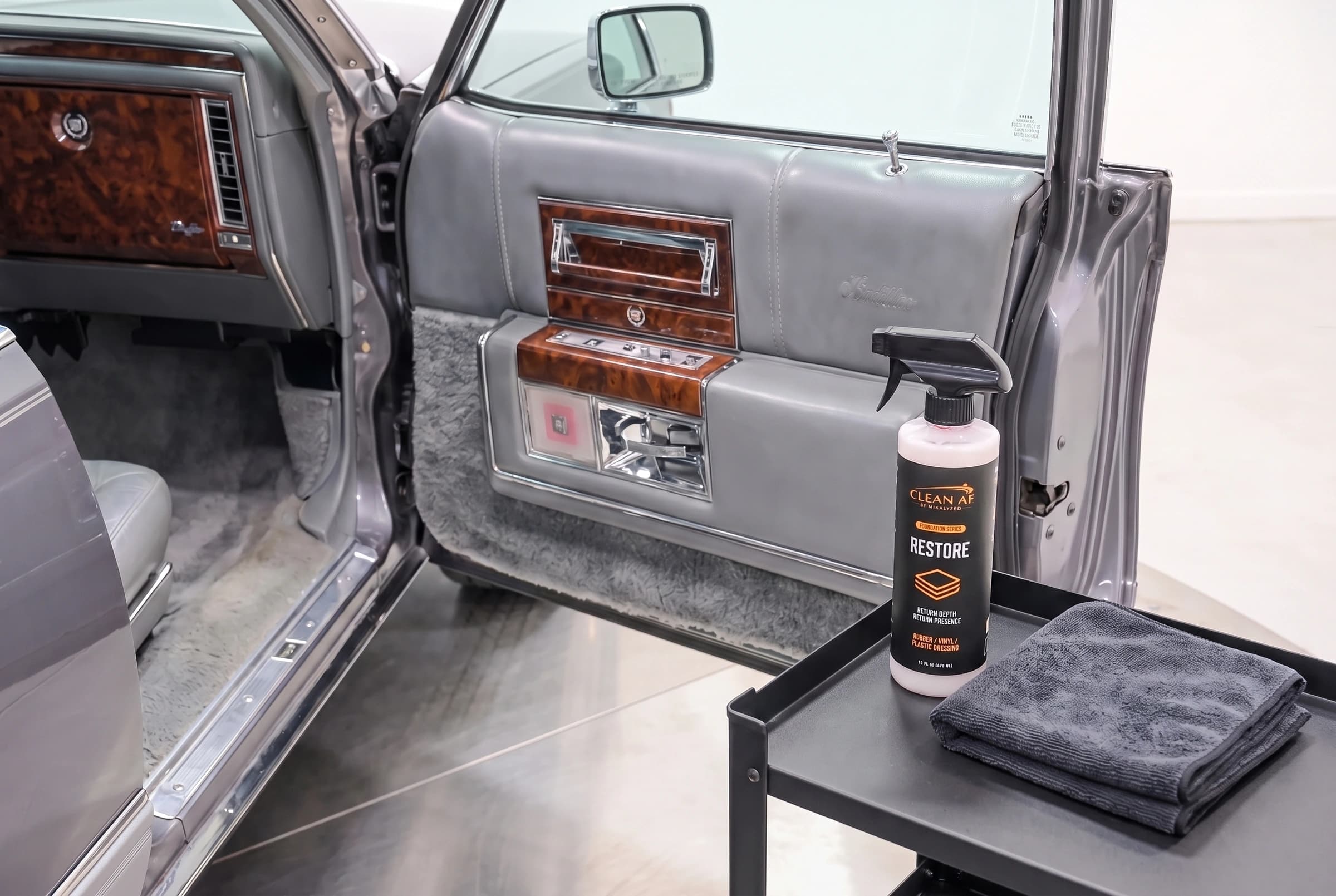 RESTORE and a folded microfiber towel beside the finished gray Cadillac vinyl door panel
